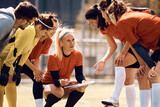 Women's soccer team and their coach going through game plan on football pitch.