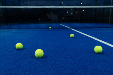 Wall Mural - five balls on a blue paddle tennis court at dusk, racket sports concept