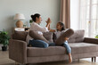 © fizkes - Happy mom and cheerful little kid giving high five after pillow fighting battle, sitting on couch, holding cushions, clapping hands, laughing, talking, playing active games. Family leisure concept