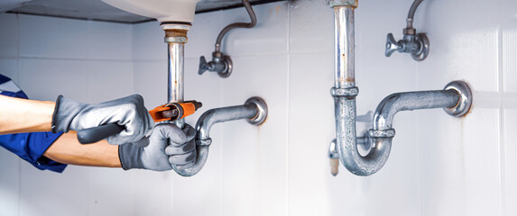 Wall Mural - Technician plumber using a wrench to repair a water pipe under the sink. Concept of maintenance, fix water plumbing leaks, replace the kitchen sink drain, cleaning clogged pipes is dirty or rusty.