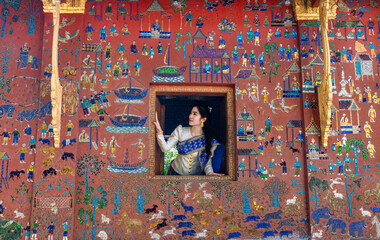 Wall Mural - Asian woman wearing a Lao national costume visits Wat Xieng Thong one of the most famous attraction place in Luang Prabang.