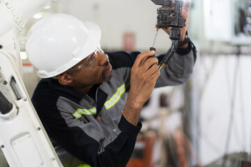 Wall Mural - African American male technician worker maintenance robotic arm with screwdriver. African American male engineer worker maintenance automatic robotic arm machine in factory.