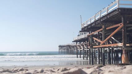 Wall Mural - Below wooden Crystal pier on piles, ocean beach water waves, California USA. Summer vacations on Mission beach, San Diego shore. Under waterfront promenade on sea coast. Seamless looped cinemagraph.