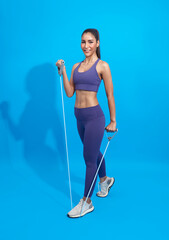 Wall Mural - Fitness asian woman in sportswear exercising with a resistance band on blue background. Attractive active female doing squatting workout burning fat.