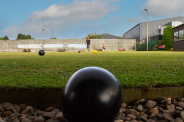 Wall Mural - Crown green bowling ball sitting in ditch at edge of green after male takes bad shot, he can be seen walking across the bowling green to check on his score as he plays in a competition.