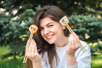 Wall Mural - A young woman eating sushi in the park, picnic in nature.