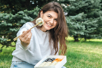 Wall Mural - A young woman eating sushi in the park, picnic in nature.