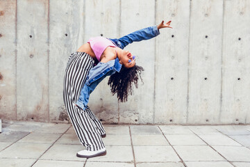 teenage woman dancing in the city outdoors, generation z trendy urban dance sport in blue jacket and glasses