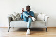 © Prostock-studio - African American Man Using Cellphone Texting Sitting On Couch Indoor