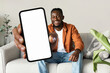 Trendy mobile phone. Happy black man holding smartphone with white empty screen, showing device to camera, mock up