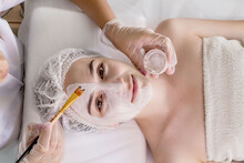 A Beautician Applies A Mask To The Skin Of A Woman's Face For Therapeutic Purposes. Rejuvenation, Acne Treatment