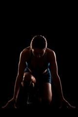 Wall Mural - Female runner in low race start position. Girl in sportswear against dark background..