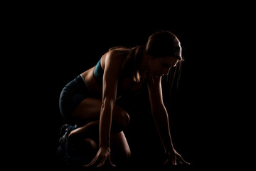 Wall Mural - Female runner in low race start position. Girl in sportswear against dark background..