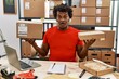 African man with curly hair working at small business ecommerce in shock face, looking skeptical and sarcastic, surprised with open mouth
