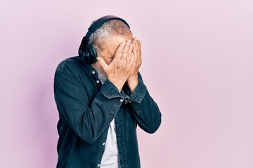 Wall Mural - Handsome senior man with beard listening to music using headphones with sad expression covering face with hands while crying. depression concept.