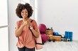 African american woman with afro hair holding yoga mat at pilates room with a big smile on face, pointing with hand finger to the side looking at the camera.
