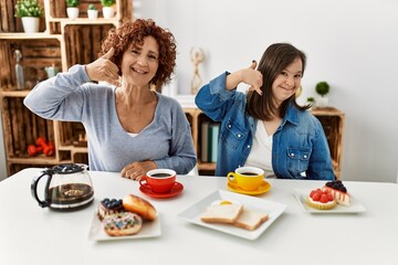 Wall Mural - Family of mother and down syndrome daughter sitting at home eating breakfast smiling doing phone gesture with hand and fingers like talking on the telephone. communicating concepts.