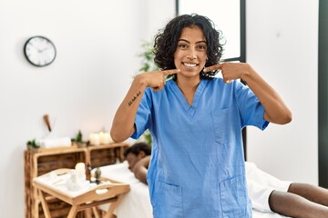 Sticker - Young therapist woman at wellness spa center smiling cheerful showing and pointing with fingers teeth and mouth. dental health concept.