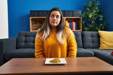 Wall Mural - Young hispanic woman eating green peas looking to side, relax profile pose with natural face and confident smile.