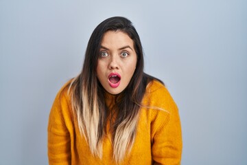 Wall Mural - Young hispanic woman standing over isolated background afraid and shocked with surprise and amazed expression, fear and excited face.