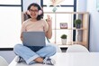 © Krakenimages.com - Young hispanic woman using laptop sitting on the table wearing headphones showing and pointing up with fingers number three while smiling confident and happy.