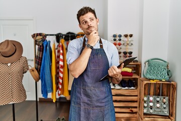 Sticker - Handsome young man working as manager at retail boutique with hand on chin thinking about question, pensive expression. smiling with thoughtful face. doubt concept.