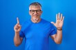 © Krakenimages.com - Hispanic man with grey hair standing over blue background showing and pointing up with fingers number six while smiling confident and happy.