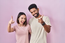 Young Hispanic Couple Together Over Pink Background Pointing Fingers To Camera With Happy And Funny Face. Good Energy And Vibes.