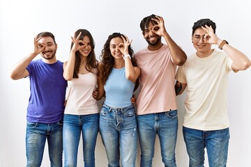 Canvas Print - Group of young people standing together over isolated background doing ok gesture with hand smiling, eye looking through fingers with happy face.