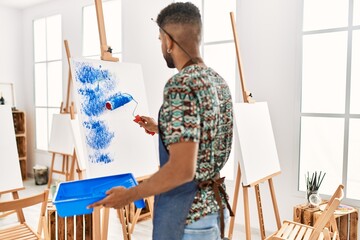 Wall Mural - Young african american artist man on back view painting with paint roller at art studio.