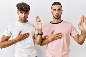 Sticker - Young gay couple standing over isolated background swearing with hand on chest and open palm, making a loyalty promise oath