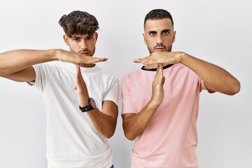 Sticker - Young gay couple standing over isolated background doing time out gesture with hands, frustrated and serious face