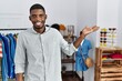 © Krakenimages.com - Young african american man working as manager at retail boutique smiling cheerful presenting and pointing with palm of hand looking at the camera.