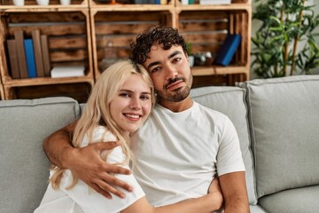 Wall Mural - Young beautiful couple sitting on the sofa and hugging at home.