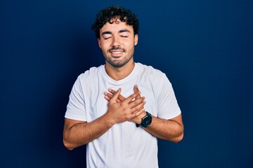 Sticker - Young hispanic man wearing casual white t shirt smiling with hands on chest with closed eyes and grateful gesture on face. health concept.