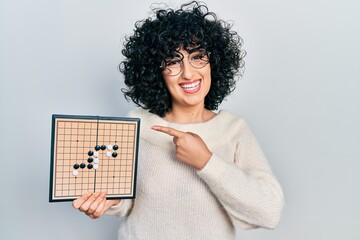 Sticker - Young middle east woman holding asian go game board smiling happy pointing with hand and finger