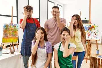 Poster - Group of five hispanic artists at art studio covering one eye with hand, confident smile on face and surprise emotion.