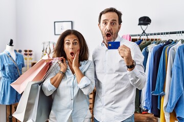 Wall Mural - Hispanic middle age couple holding shopping bags and credit card afraid and shocked, surprise and amazed expression with hands on face