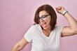 © Krakenimages.com - Middle age hispanic woman standing over pink background dancing happy and cheerful, smiling moving casual and confident listening to music