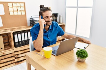 Wall Mural - Handsome hispanic man working with laptop speaking on the phone at the office