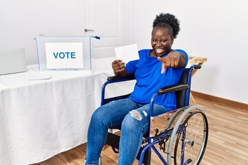 Sticker - Young african woman sitting on wheelchair voting putting envelop in ballot box pointing to you and the camera with fingers, smiling positive and cheerful