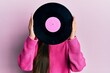 © Krakenimages.com - Woman holding retro vinyl disc covering face over pink background
