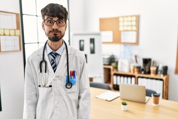 Poster - Hispanic man with beard wearing doctor uniform and stethoscope at the office puffing cheeks with funny face. mouth inflated with air, crazy expression.