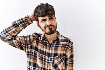 Wall Mural - Hispanic man with beard standing over isolated background confuse and wonder about question. uncertain with doubt, thinking with hand on head. pensive concept.