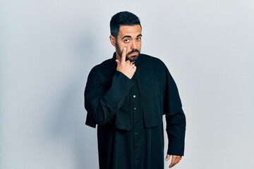 Poster - Handsome hispanic man with beard wearing catholic priest robe pointing to the eye watching you gesture, suspicious expression