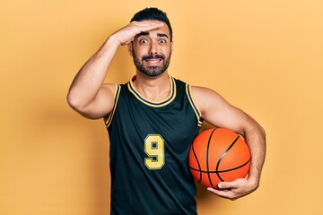 Wall Mural - Handsome hispanic man with beard holding basketball ball stressed and frustrated with hand on head, surprised and angry face