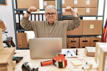 Wall Mural - Senior caucasian man working at small business ecommerce with laptop showing arms muscles smiling proud. fitness concept.