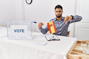 Poster - Young handsome man with beard at political campaign election holding spain flag with angry face, negative sign showing dislike with thumbs down, rejection concept