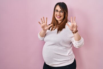 Poster - Pregnant woman standing over pink background showing and pointing up with fingers number eight while smiling confident and happy.