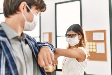 Wall Mural - Two business workers wearing medical mask doing elbow coronavirus handshake at the office.